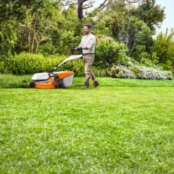 Mężczyzna kosi trawę w ogrodzie kosiarką spalinową STIHL.