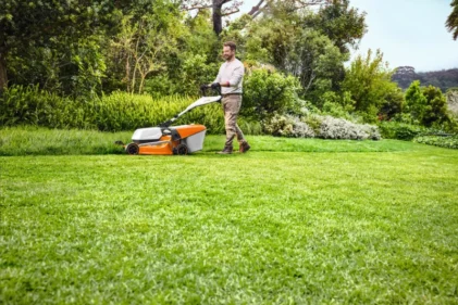 Mężczyzna kosi trawę w ogrodzie kosiarką spalinową STIHL.