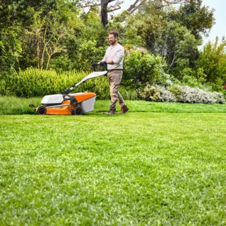 Mężczyzna kosi trawę w ogrodzie kosiarką spalinową STIHL.